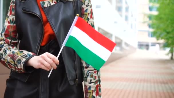 Unrecognizable woman holding Hungarian flag. Girl walking down street with national flag of Hungary — Vídeo de stock