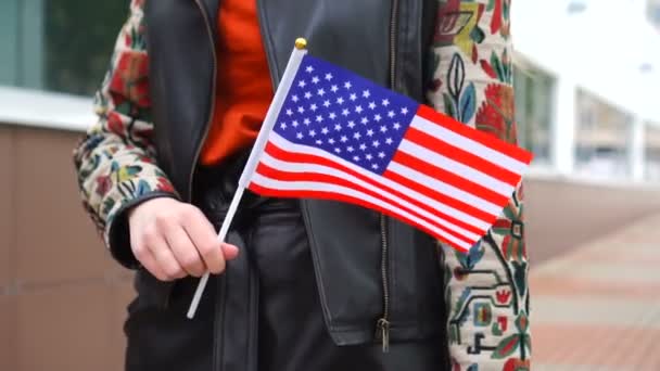 Unrecognizable woman holding US flag. Girl walking down street with national flag of United States of America — Vídeo de stock