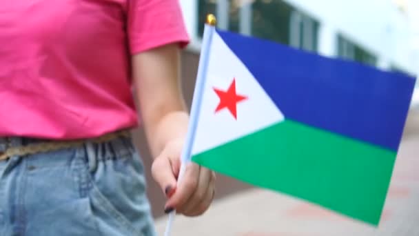 Mujer irreconocible sosteniendo la bandera de Djibouti. Chica caminando por la calle con la bandera nacional de Yibuti — Vídeos de Stock