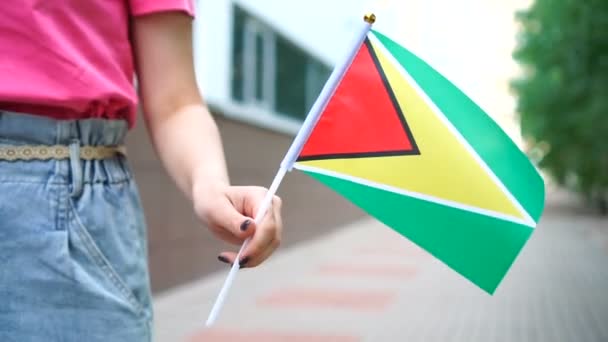 Elinde Guyanese bayrağı tutan tanınmayan bir kadın. Guyana 'nın ulusal bayrağıyla sokakta yürüyen bir kız — Stok video