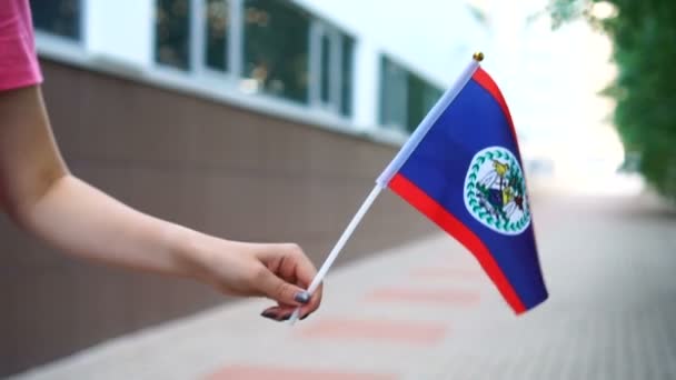 Nierozpoznana kobieta trzymająca flagę Belizean. Dziewczyna idzie ulicą z flagą narodową Belize — Wideo stockowe