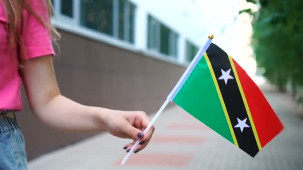 Eine unkenntliche Frau mit einer kittizianischen oder nevisischen Fahne. Mädchen läuft mit Nationalflagge von St. Kitts und Nevis die Straße entlang — Stockvideo