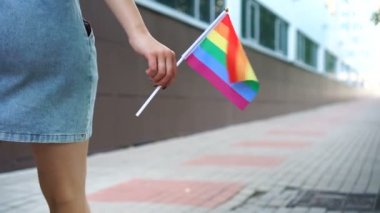 Eşcinsel gökkuşağı bayrağıyla sokakta yürüyen tanınmayan bir kadın.