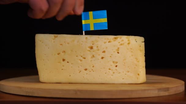 Mans hand sätta liten i storlek tandpetare med svensk flagga på ost. — Stockvideo