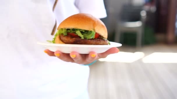 Hamburguesa lista para comer. Hamburguesa jugosa de mano con carne de res, lechuga y cebolla en plato blanco — Vídeo de stock