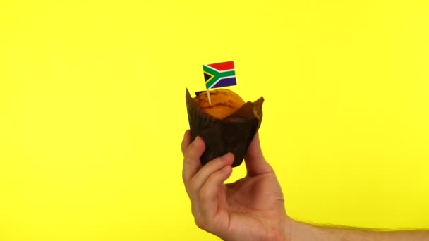 Cupcake com bandeira sul-africana na palma da mão masculina contra fundo amarelo — Vídeo de Stock