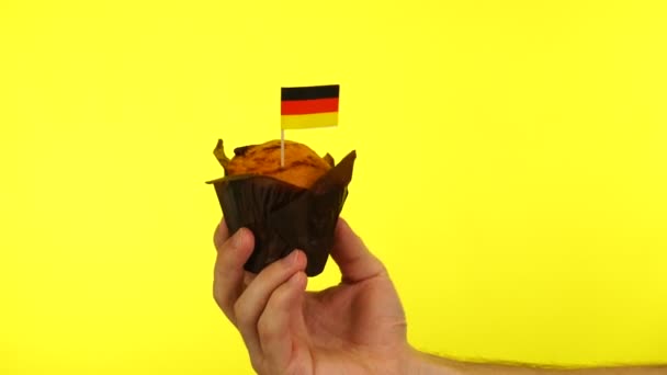 Кекс с немецким флагом на мужской ладони на желтом фоне — стоковое видео