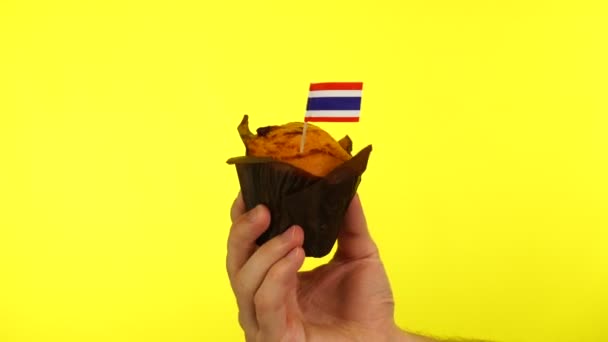 Cupcake com bandeira tailandesa na palma do macho contra fundo amarelo — Vídeo de Stock