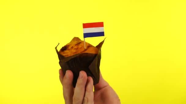 Кекс с голландским флагом на мужской ладони на желтом фоне — стоковое видео