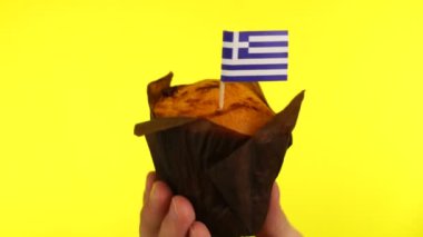 Sarı arka planda erkek avucunda Yunan bayrağı olan kek