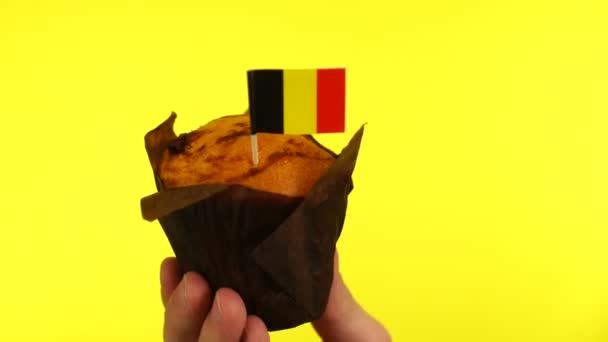 Кекс с бельгийским флагом на мужской ладони на желтом фоне — стоковое видео