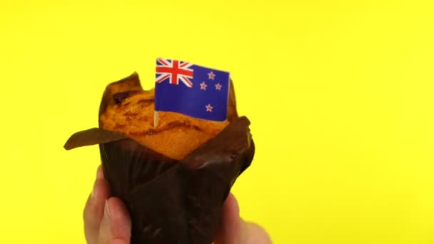 Кекс с флагом Новой Зеландии на мужской ладони на желтом фоне — стоковое видео
