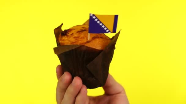 Cupcake with Bosnian and Herzegovinian flag on male palm against yellow background — Stock Video