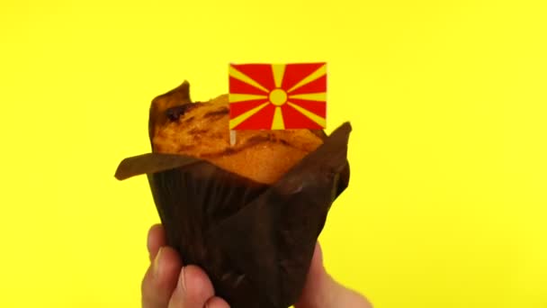 Кекс с македонским флагом на мужской ладони на желтом фоне — стоковое видео