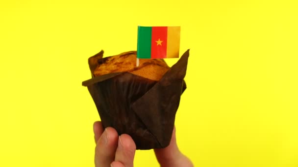 Кекс с флагом Камеруна на мужской ладони на желтом фоне — стоковое видео