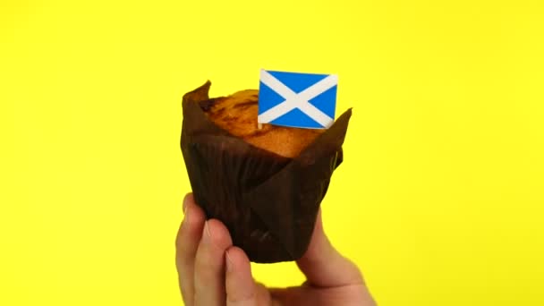 Кекс с шотландским флагом на мужской ладони на желтом фоне — стоковое видео
