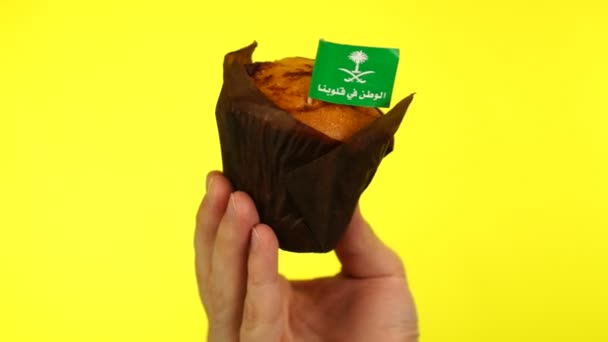 Cupcake met Saoedische vlag op mannelijke palm tegen gele achtergrond — Stockvideo