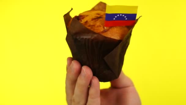 Кекс с венесуэльским флагом на мужской ладони на жёлтом фоне — стоковое видео