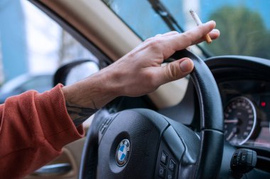 Araba sürerken yanan bir sigarayı tutan el.