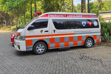 Jakarta - 6 Ekim 2025: Medika Prakarsa ambulansı, ağaçların yakınındaki tuğla kaldırımda kareli üniforma parketmiş.