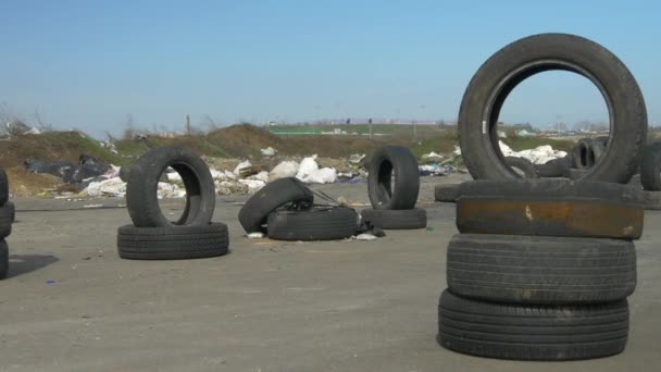 Staré použité pneumatiky jsou navrstvené na zpevněné silnici. Spousta trosek na pozadí. Vítr hýbe kousky smetí. Zářivý slunečný den. — Stock video