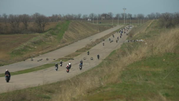 Många cyklister på motorcyklar ridande bort på en lång rak väg med kullar. — Stockvideo