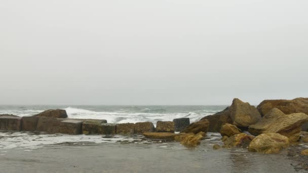 Plage de sable avec mer agitée rugueuse, rochers jaunes, nuages gris denses couvrant le ciel . — Video