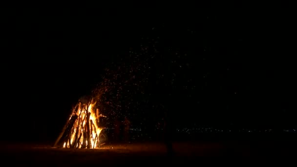 砂の上の巨大な焚き火。火花がたくさん。モバイル デバイスを持つ男のシルエット. — ストック動画
