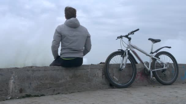 自転車で孤独な男が巨大な嵐の中古い高コンクリート桟橋に座っています。. — ストック動画