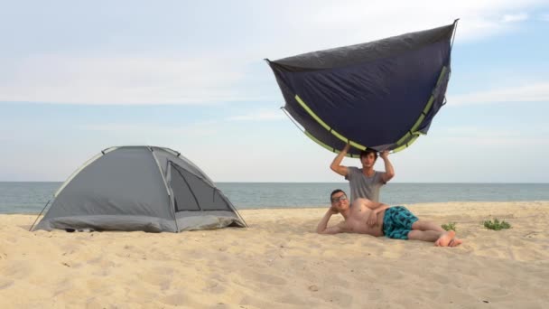 Dois homens na praia a brincar com tendas. Instalando tendas no acampamento perto do mar . — Vídeo de Stock