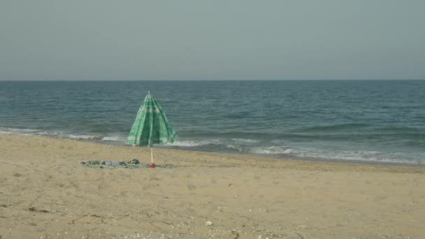 Lonely beach paraply i sand nära havet. Vinden blåser på paraply och handduk. — Stockvideo