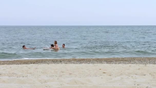 Young people are swimming and playing in sea of turquoise near the sandy beach. — Stock Video