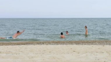 Gençler kumlu plaja yakın turkuaz denizde yüzüyor.