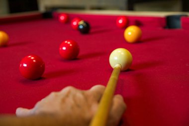 Bir oyuncu nişan alırken bilardo ıstakasının ucuna özenle odaklanmış bir bilardo oyunu. 