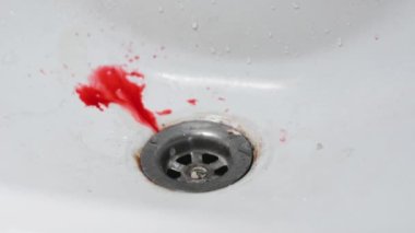 İnsan kanı yavaşça damlar ve temiz beyaz bir lavabonun üzerine yayılır.