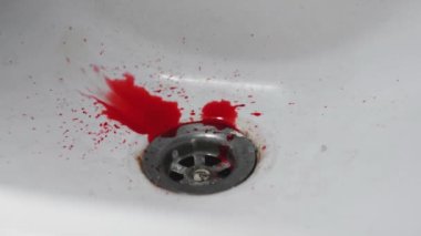 İnsan kanı yavaşça damlar ve temiz beyaz bir lavabonun üzerine yayılır.