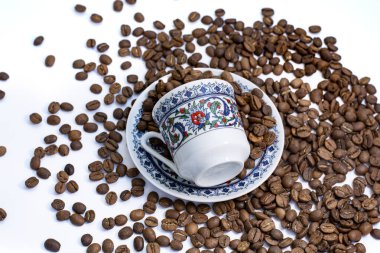 Kahve çekirdeği dolu kahve fincanı beyaz masada.