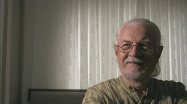 Sabah Işığıyla aydınlatılan Sakin Bir Yuvadaki Yaşlı, Beyaz Saçlı ve Sakallı Adam portresi. Gözlerini yukarı kaldırır ve tüm samimiyetiyle gülümser sonra da kahvesini siyah bardaktan yudumlar..