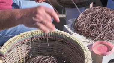 Bir balıkçının ellerinin detaylı bir yakın çekimi uzun hat (el hattı) müdahalesi hazırlıyor. Adam ana hatta titizlikle çalışıyor ve dişlileri düzenlemek için geleneksel dokuma sepetine sarıyor..