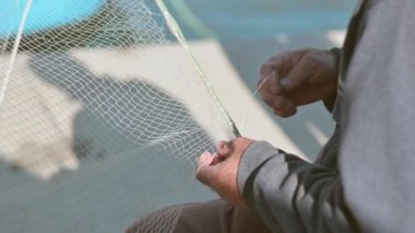 Ağı tamir eden bir balıkçının yakın plan fotoğrafı, geleneksel balıkçılık kültürünü ve el işçiliğini temsil ediyor..