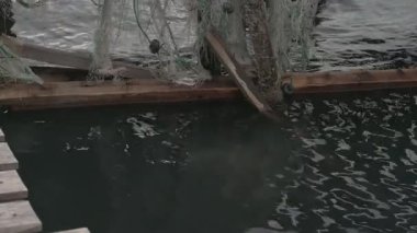 Fırtınadan sonra sürüklenen kırık balık ağlarının ve plastik şamandıraların gerçek görüntüleri. Deniz kirliliği ve sürdürülebilirlik sorunlarını gösteren otantik sahil çevre sahnesi. Belgesel yakalama, doğal süreç, yapay zeka değil..