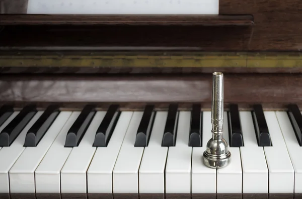 A trumpet mouthpiece upon the piano keys, close up