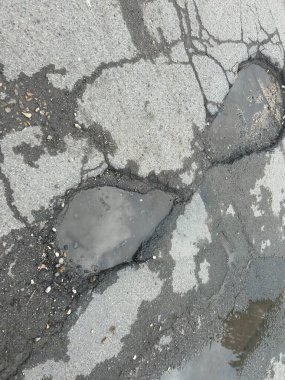 Engebeli çukurlar ve yolda ıslak su birikintisi ve enkaz ile çatlamış asfalt