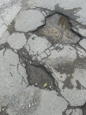 Engebeli çukurlar ve yolda ıslak su birikintisi ve enkaz ile çatlamış asfalt