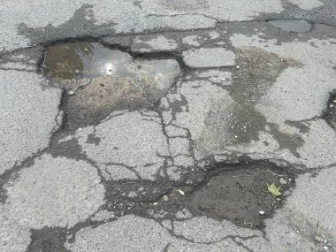 Engebeli çukurlar ve yolda ıslak su birikintisi ve enkaz ile çatlamış asfalt