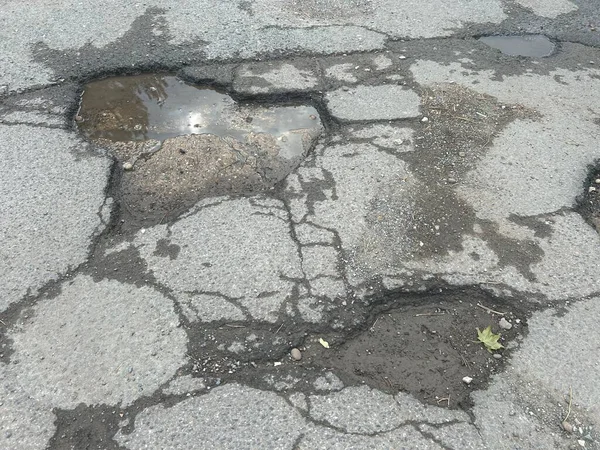 Engebeli çukurlar ve yolda ıslak su birikintisi ve enkaz ile çatlamış asfalt