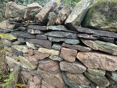 Yıpranmış doğal dokusu olan katmanlı kayalardan inşa edilmiş engebeli bir taş duvar.