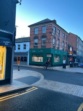 Loughborough, Leicestershire, İngiltere, 20 Aralık 2025, South Street, Urban Street Scene with Brick Building, Green Shopfront, and Cycling Pedestrian