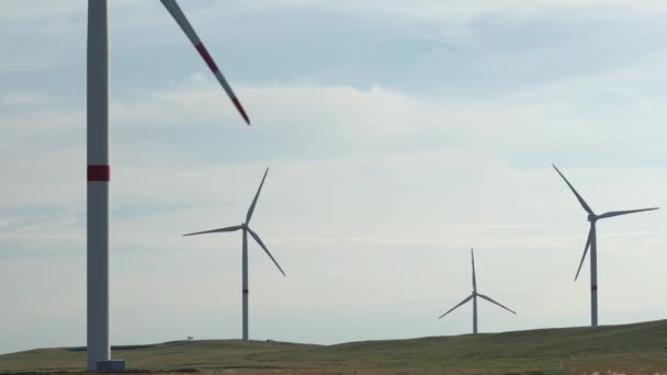 Bewegen Sie die Flügel einer großen Windkraftanlage auf einem Feld vor dem Hintergrund eines orangefarbenen Sonnenuntergangs am Horizont mit einem wunderschönen Hügel. Alternative Energiequellen. Windiger Park. Ökologische Energie.Industrie — Stockvideo