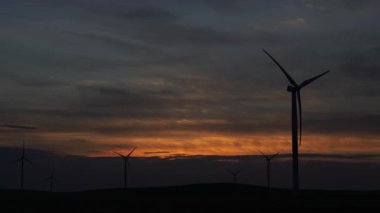 Bir tarladaki büyük bir rüzgar türbininin pervanelerini ufuktaki turuncu günbatımının arka planına doğru hareket ettir. Alternatif enerji kaynakları. Rüzgarlı park. Ekolojik enerji. Sanayi.